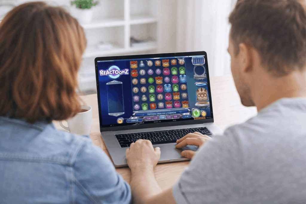 Two people sitting together at a table, viewing the Reactoonz slot game on a laptop screen