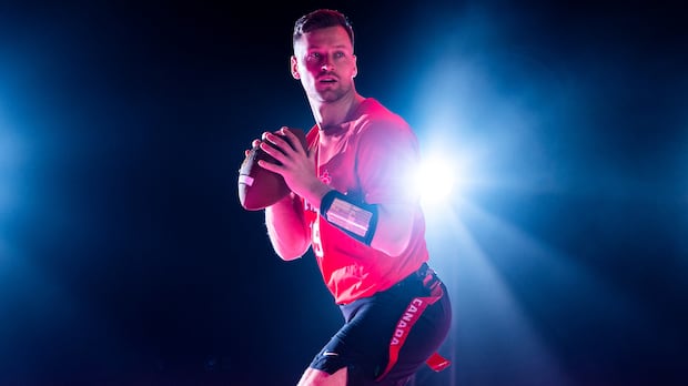 Men’s flag football player gripping football on field with bright stadium lights shining behind him