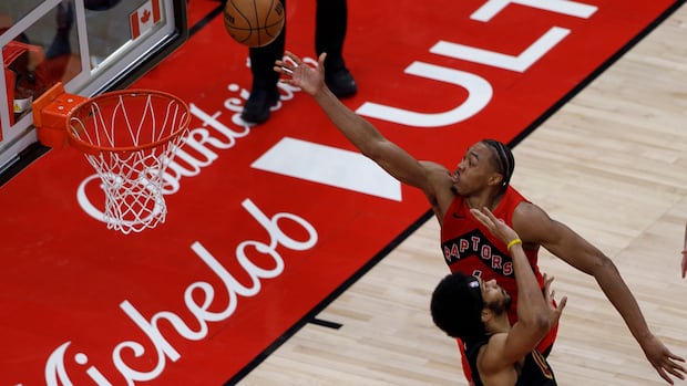 Toronto Raptors player shooting a basketball as a Cleveland Cavaliers defender attempts to block the shot