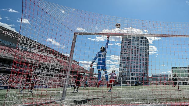 Atlético Ottawa goalie jumps to catch a ball kicked high during a sunny home game against Vancouver FC