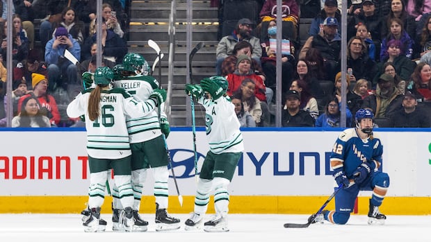 Vancouver Goldeneyes hockey players celebrate a goal as an opposing team member watches on the ice
