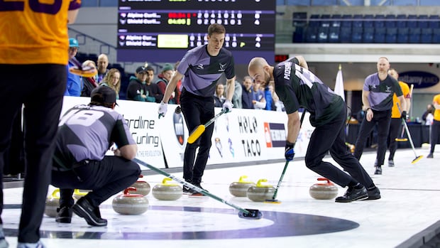 Curlers sliding stones on ice as teammates sweep vigorously to guide the stone during a competitive match