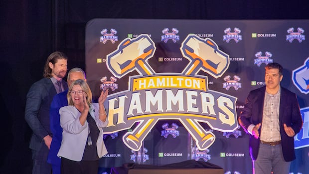 Four men in suits standing beside a large Hamilton Hammers logo with two crossed hammers on cardboard display