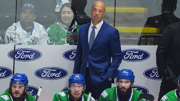 Abbotsford Canucks coach Manny Malhotra watches game action behind players Sammy Blais, Jonathan Lekkerimaki, and Phillip Di Giuseppe