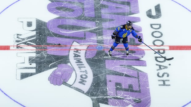 Hockey player skating with puck at centre ice during a game