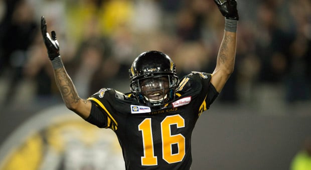 Brandon Banks smiling and holding a Hamilton Tiger-Cats jersey during his Hall of Fame induction announcement