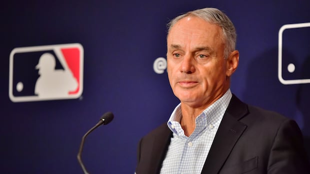 MLB commissioner speaking at a podium during a press conference on proposed salary cap