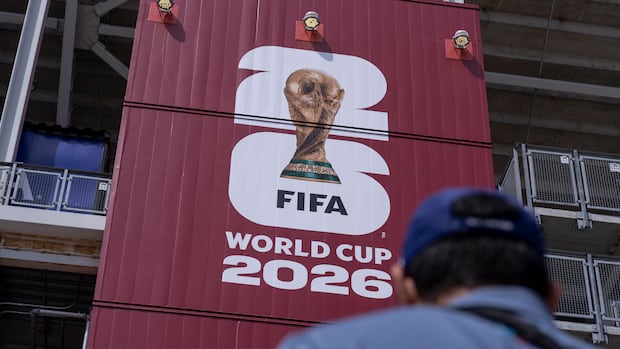 Man walking toward BMO Field with a large FIFA 2026 World Cup banner hanging outside on a sunny day