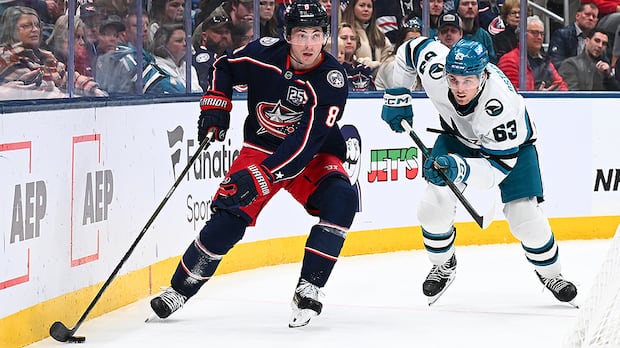 Zach Werenski of Blue Jackets skates with puck while Zack Ostapchuk of Sharks defends at Nationwide Arena